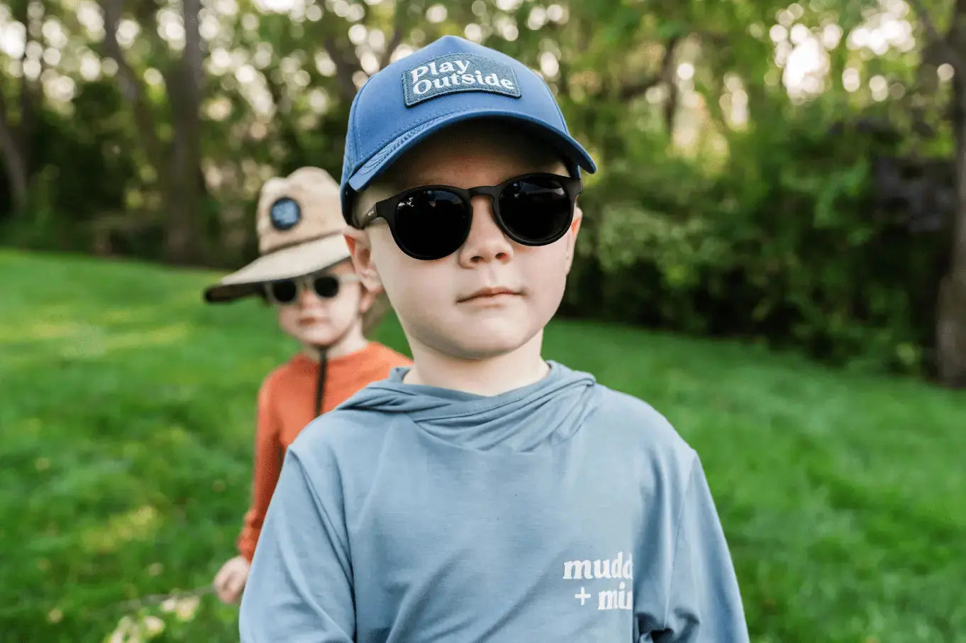 Child wearing The ONE Shirt in Teal, enjoying an outdoor adventure with breathable, all-weather sun-safe comfort. Wearing the Play outside snapback and other child in the back
