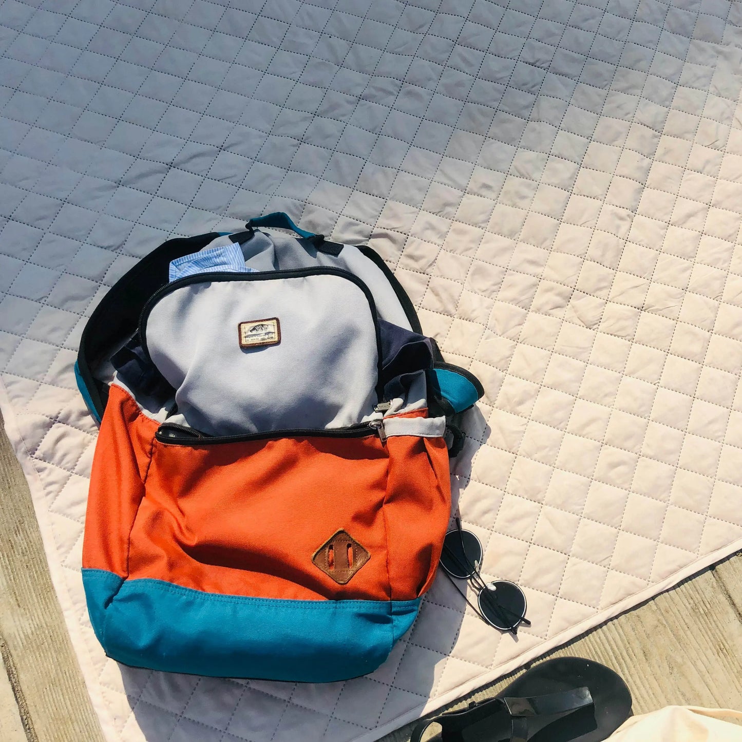 A backpack filled with summer essentials like sunscreen, water bottles, sun hats, and a folded ONE Shirt ready for a weekend adventure.