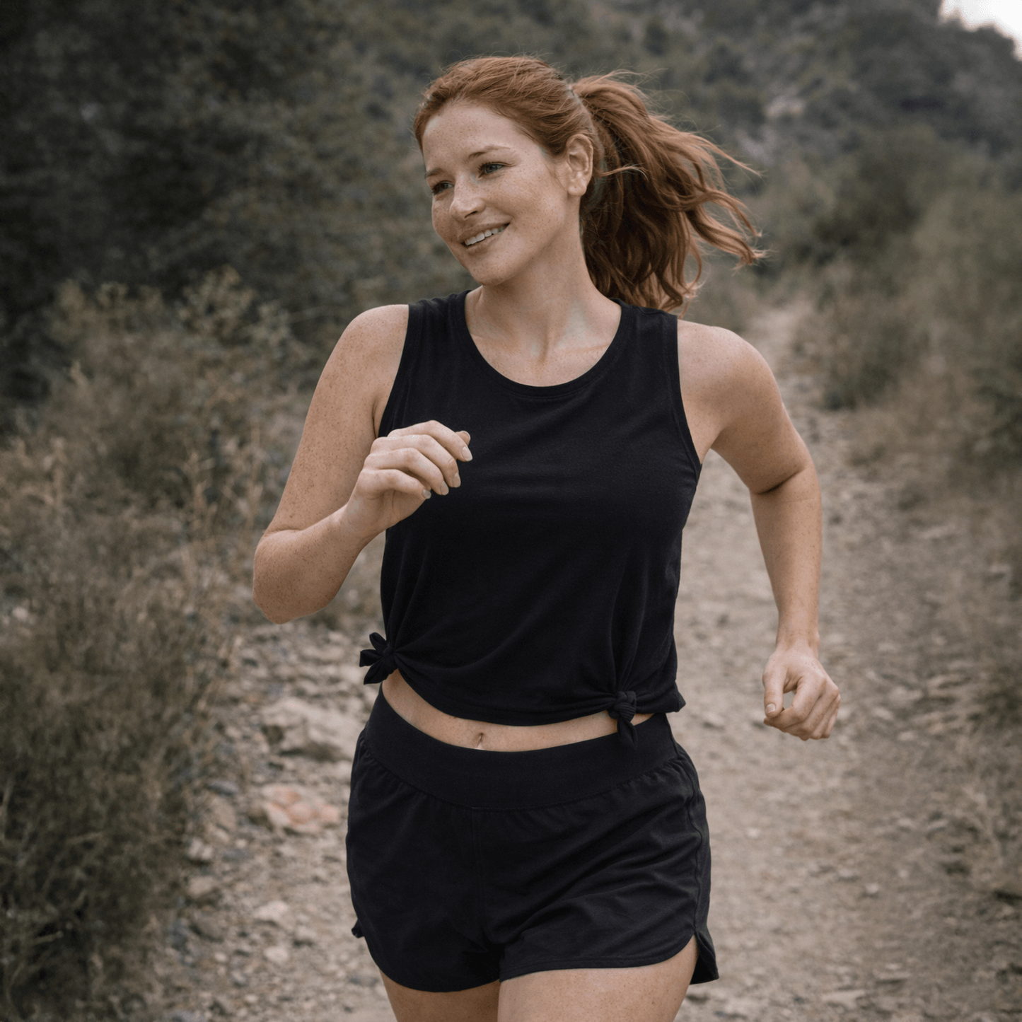 Woman running outdoors on a dirt path with greenery in the background