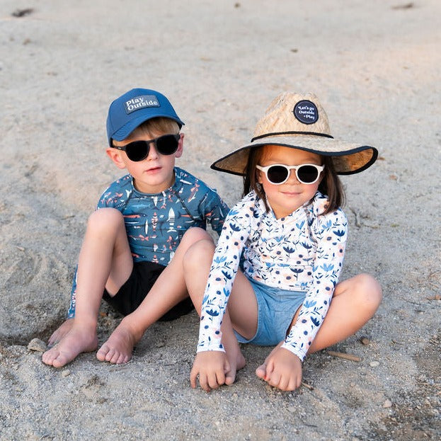 Girl and Boy at the beach sporting Muddy + Mind rash guards, hats and sunglasses. Sun safe UPF 50+ at the beach