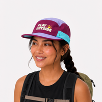 Woman wearing a colorful cap with 'Play Outside' text and a backpack on a white background