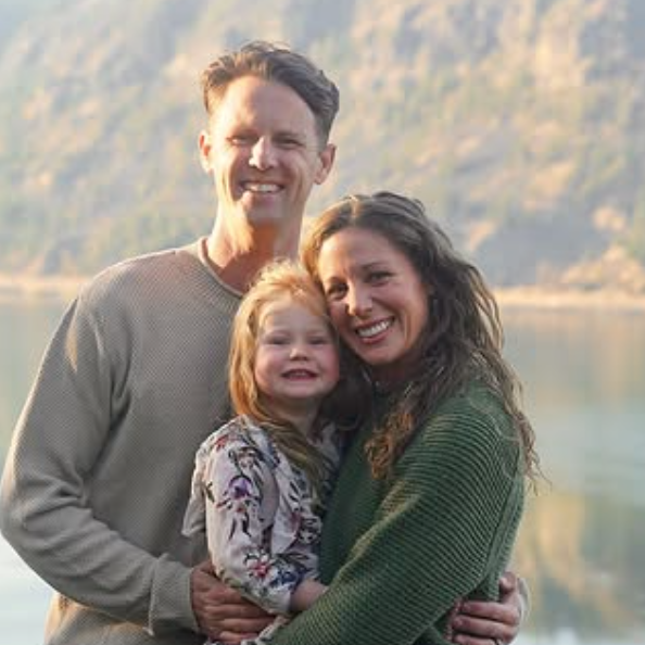 Family of three smiling in front of a scenic mountain landscape