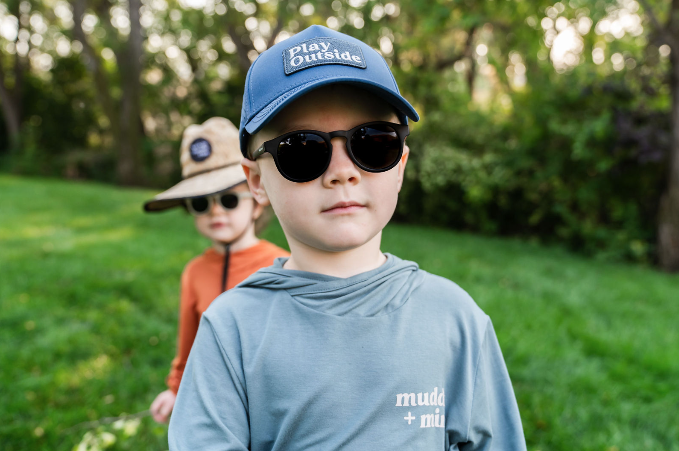 Child wearing The ONE Shirt in Teal, enjoying an outdoor adventure with breathable, all-weather sun-safe comfort. Wearing the Play outside snapback and other child in the back