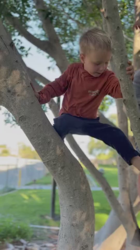toddler boy climbing a tree with his bamboo sun shirt by play outside