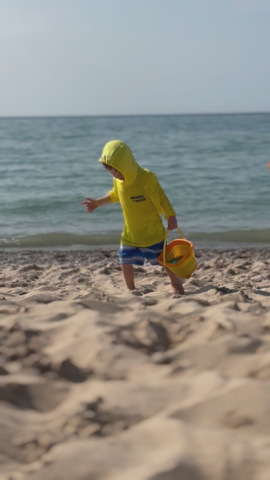 boy at the beach with his safety yellow sun shirt by play outside